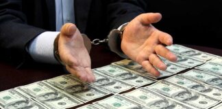 Handcuffed hands over a table of hundred-dollar bills.