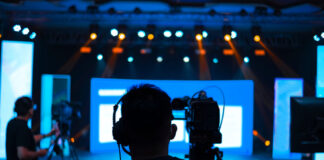 Camera operators filming a brightly lit stage.