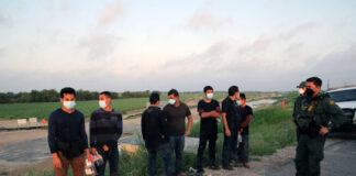 People wearing masks stand near border patrol agents outdoors.