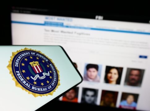 FBI logo on phone with wanted fugitives list behind.