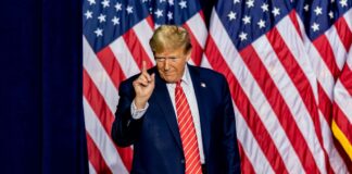Man standing before American flags wearing suit and tie