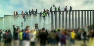 Crowd and people climbing large border wall during protest.