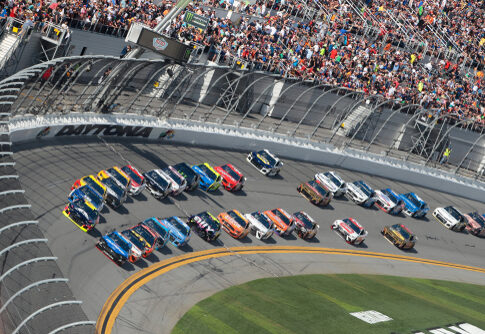 NASCAR race at Daytona Speedway with cheering spectators.