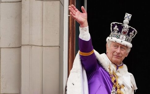 King Charles III in coronation attire waving.