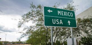 Direction sign for Mexico left, USA straight ahead.