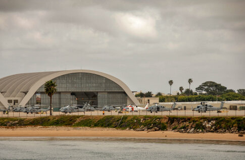 Hangar with military helicopters near a beach.