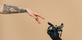 Tattoo artist's hand holding tattoo machine, reaching tattooed arm.