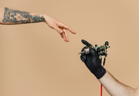 Tattoo artist's hand holding tattoo machine, reaching tattooed arm.