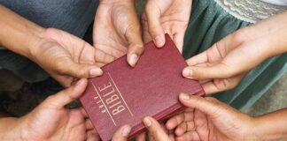 Multiple hands holding a red Bible together.