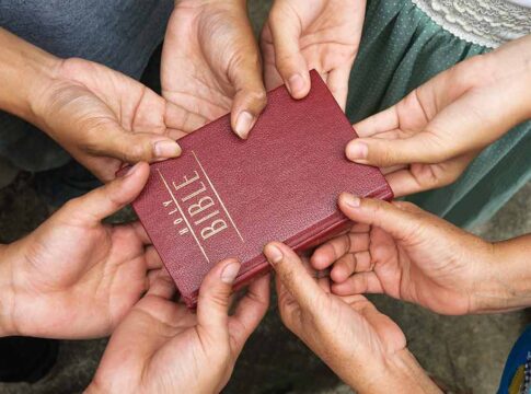 Multiple hands holding a red Bible together.