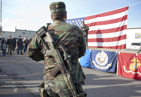 Soldier stands with rifle in front of American flag.