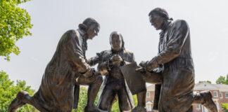 Bronze statues of three men signing a document outdoors.