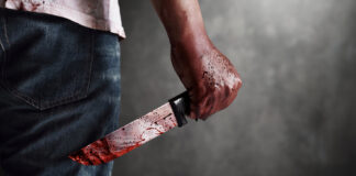 Person holding bloodstained knife behind back.