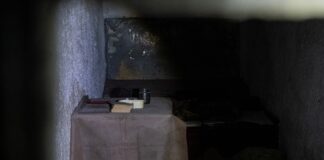 Dimly lit prison cell with small table and items.