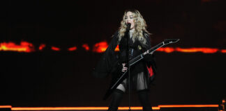 Woman playing electric guitar on stage with dramatic lighting.