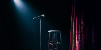 Empty stage with microphone and stool under spotlight.