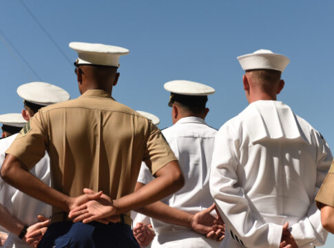 People in military uniforms standing with hands behind backs.