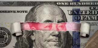 Torn dollar revealing Chinese yuan behind Benjamin Franklin's eyes.