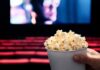 Person holding popcorn in empty movie theater.