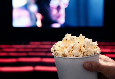 Person holding popcorn in empty movie theater.
