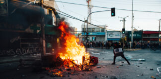 Person near large street fire during protest.