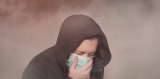 Person with hood and mask coughing in foggy setting.