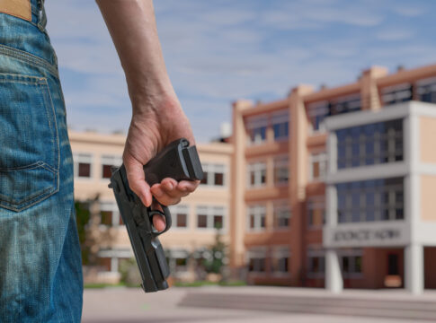 Person holding gun near school building outside