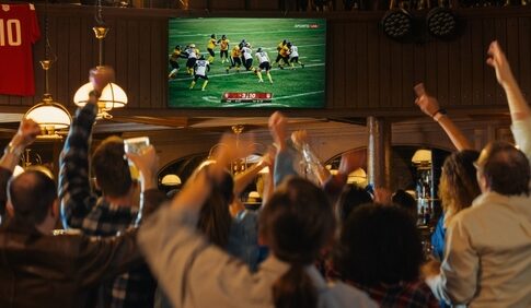 People cheering while watching football game in a bar.