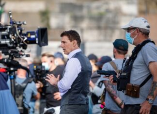 Film crew on set with man in gray vest.