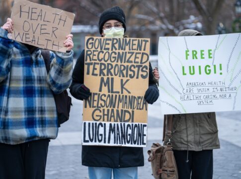 Three people holding protest signs in a park