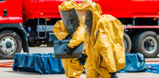 Workers in hazmat suits carrying a black container.