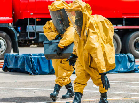 Workers in hazmat suits carrying a black container.