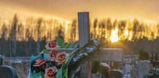 Wooden cross with flowers at sunset in a cemetery.
