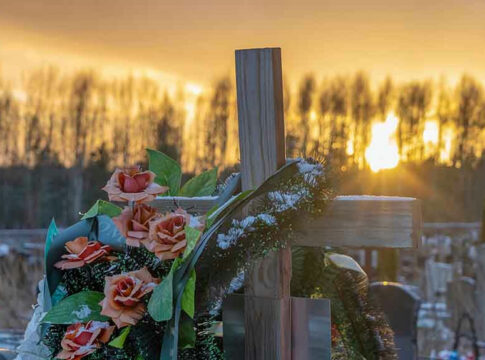 Wooden cross with flowers at sunset in a cemetery.