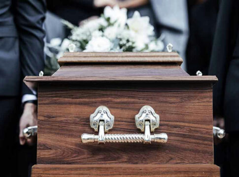 Pallbearers carrying a wooden coffin with white flowers.