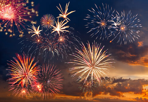 Colorful fireworks display against a darkening evening sky.