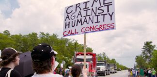 Person holding protest sign near trucks on road