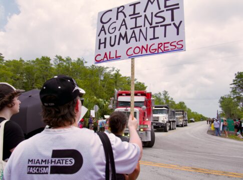 Person holding protest sign near trucks on road