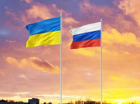 Ukrainian and Russian flags against a sunset sky.