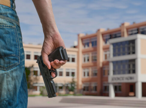 Person holding gun near school building outside