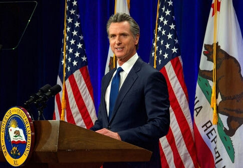 Governor Gavin Newsom speaks at podium with flags behind.