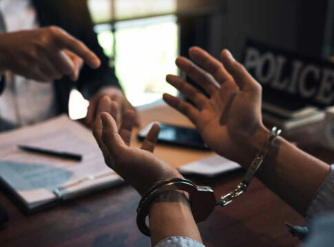 Handcuffed person is questioned by a police officer.