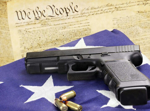 Gun and bullets on American flag with Constitution background.