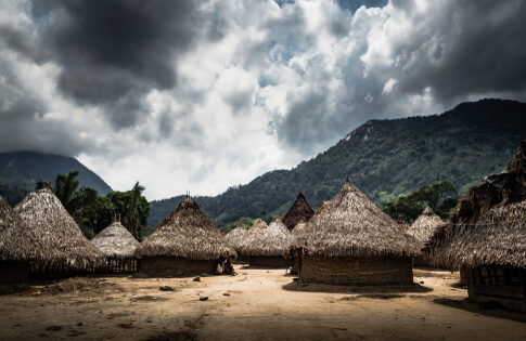 A rural village with thatched huts set against a mountainous backdrop under a cloudy sky