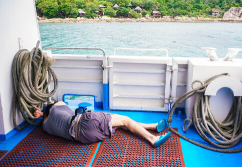 A man lying on the deck of a boat surrounded by fishing ropes with a view of the ocean