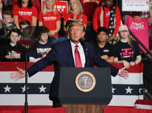 Man speaking at a rally with crowd behind.