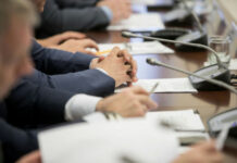 Business meeting participants with hands clasped at a conference table with microphones