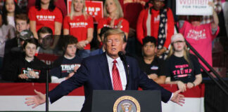 Man speaking at a rally with crowd behind.
