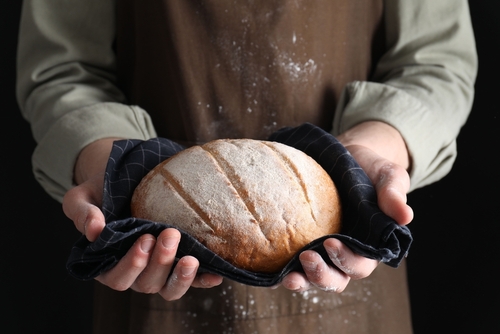 Woman,Holding,Freshly,Baked,Bread,On,Black,Background,,Closeup Person holding a freshly baked loaf of bread in a cloth